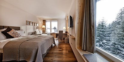 Hotels an der Piste - Suite mit offenem Kamin - Doppelzimmer "Tgiasa da Lenn". Moderne Naturmaterialien, Erd-, Gras-, Holz- und Steinfarben im Innern verschmelzen mit der Gebirgswelt, die sich vor den grossen Fenstern auftut. Das alpine Design ist ehrlich und wertvoll zugleich – wie die Natur. - Valbella Resort
