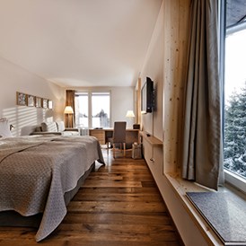 Skihotel: Doppelzimmer "Tgiasa da Lenn". Moderne Naturmaterialien, Erd-, Gras-, Holz- und Steinfarben im Innern verschmelzen mit der Gebirgswelt, die sich vor den grossen Fenstern auftut. Das alpine Design ist ehrlich und wertvoll zugleich – wie die Natur. - Valbella Resort