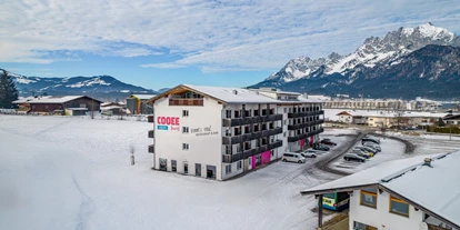 Hotels an der Piste - Verpflegung: Halbpension - Itter - Außenaufnahme des COOEE alpin Hotels Kitzbüheler Alpen mit dem Wilden Kaiser im Hintergrund - COOEE alpin Hotel Kitzbüheler Alpen