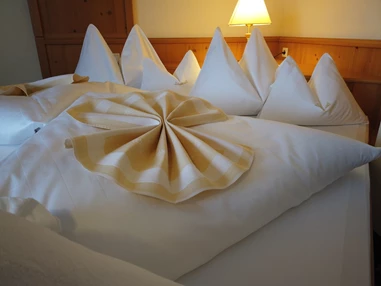 Skihotel: Das Bett in Ihrem Hotelzimmer in Obertauern ist mit hochwertiger Wäsche, die in der Inhouse Wäscherei gewaschen wird, ausgestattet. Die frische, saubere Bettdecke und die weichen Kissen laden Sie ein, sich nach einem aktiven Tag im Schnee hinzulegen und sich in die wohlige Wärme zu kuscheln. - Hotel Koch